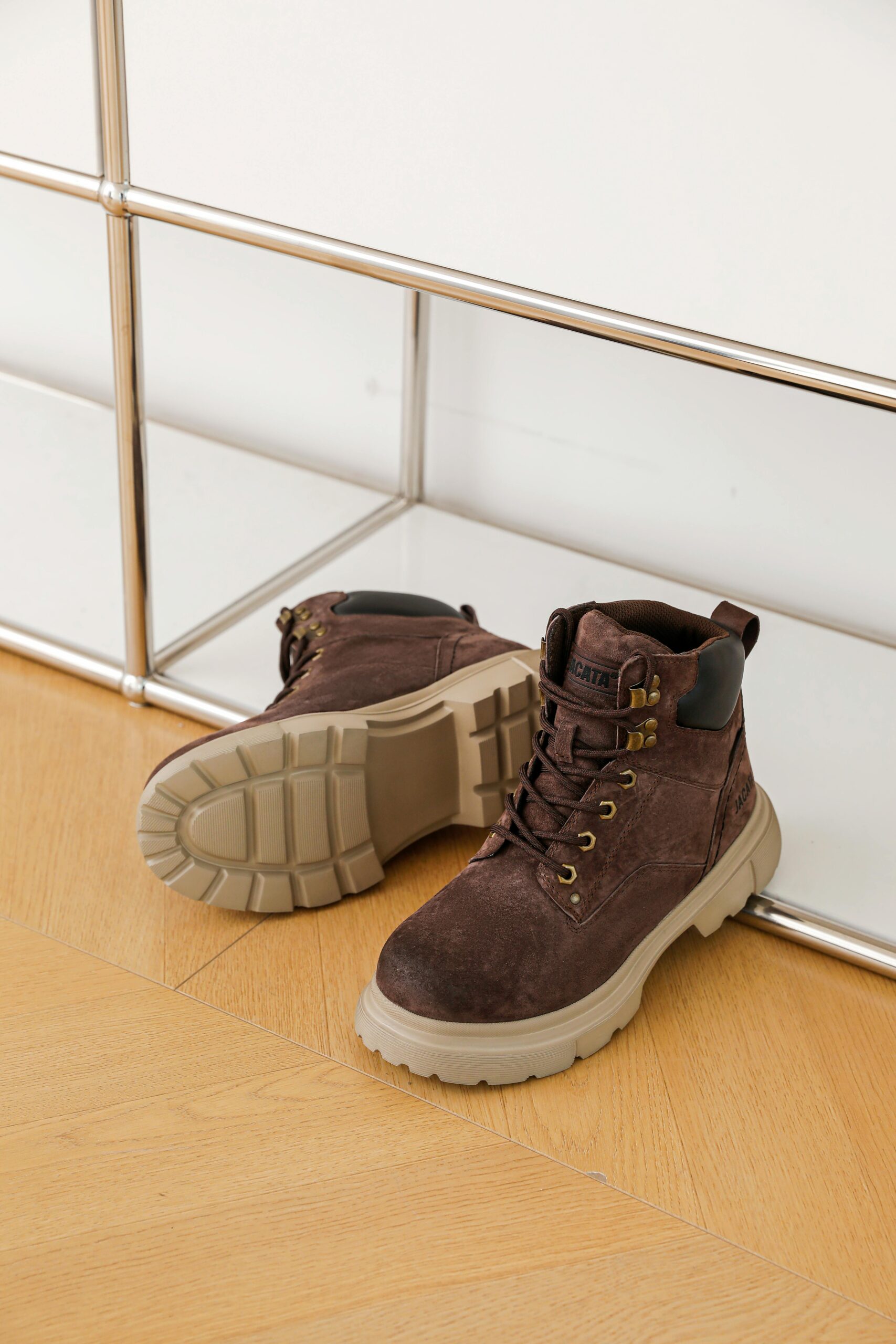 High-quality brown leather boots with thick soles on a wooden floor.