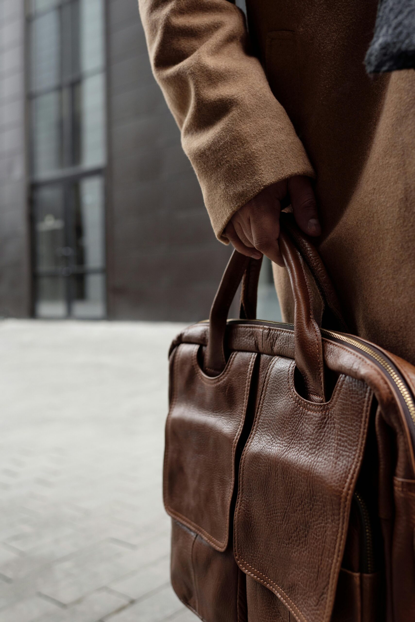 A person holding a brown leather bag, showcasing fashion and style in a city environment.